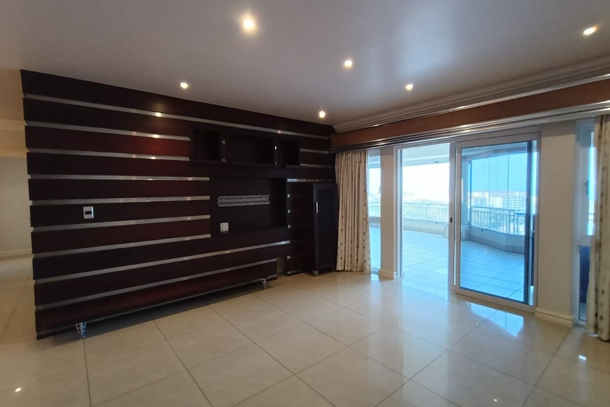 Spacious living area featuring large format floor tiles, recessed lighting, and a custom built-in media wall, with direct access to a balcony.
