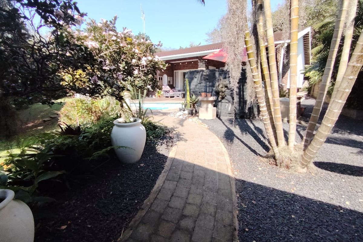 A landscaped rear garden featuring a brick paved pathway leading towards a swimming pool and a decorative rock feature.