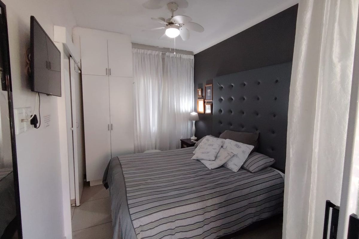 A well-maintained bedroom featuring built-in cupboards, tiled flooring, and a ceiling fan, offering a comfortable and functional living space.