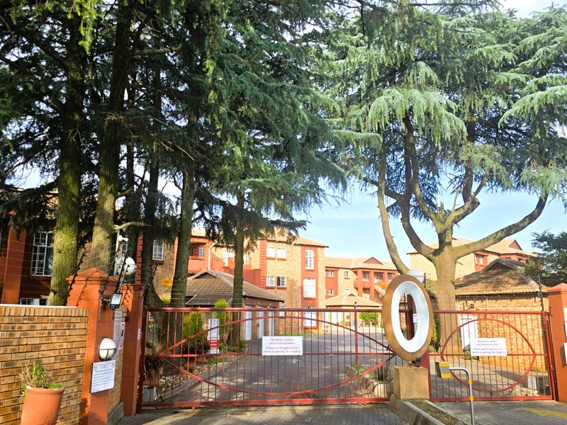 Secure gated entrance to the apartment complex featuring brick perimeter walls, electric fencing, and a paved driveway access point.