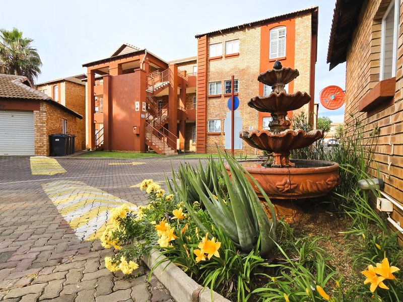 Exterior view of an apartment complex featuring brick facades, a paved driveway, a garage, and a decorative fountain in the foreground.