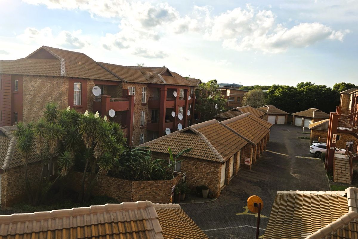 An elevated view of the apartment complex featuring face-brick buildings, tiled roofing, and a paved garage area.
