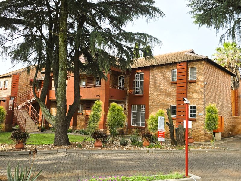 Front elevation of a multi-story apartment complex featuring face brick construction, tiled roofing, and an external staircase set within a landscaped garden area.