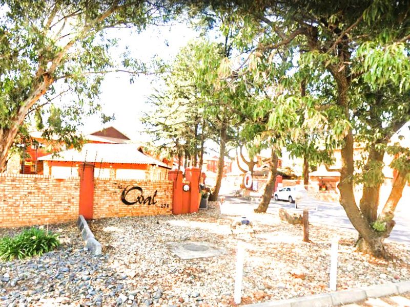 Front entrance view of the apartment complex featuring a brick boundary wall, electric fencing, and mature landscaping.