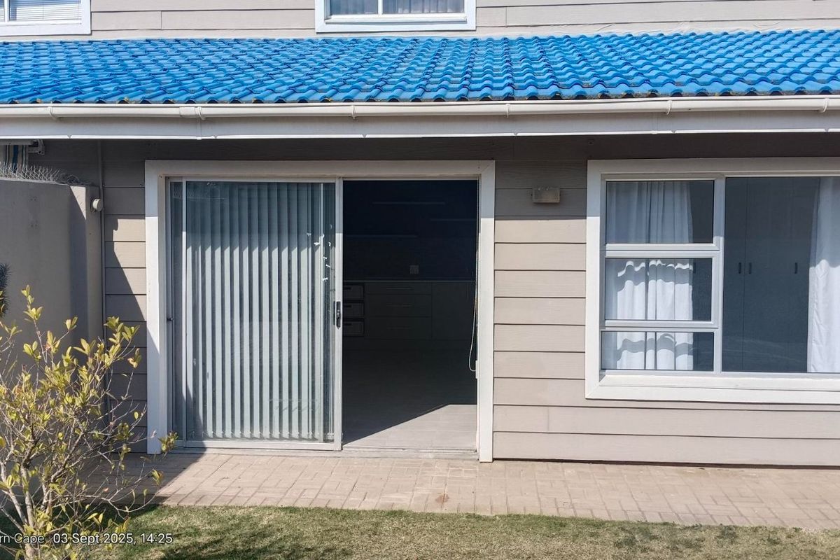 Rear exterior view of the property featuring a paved patio area, sliding glass doors, and blue tiled roof.