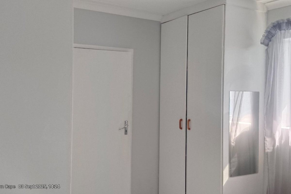A bedroom featuring built-in cupboards and a window with sheer curtains.