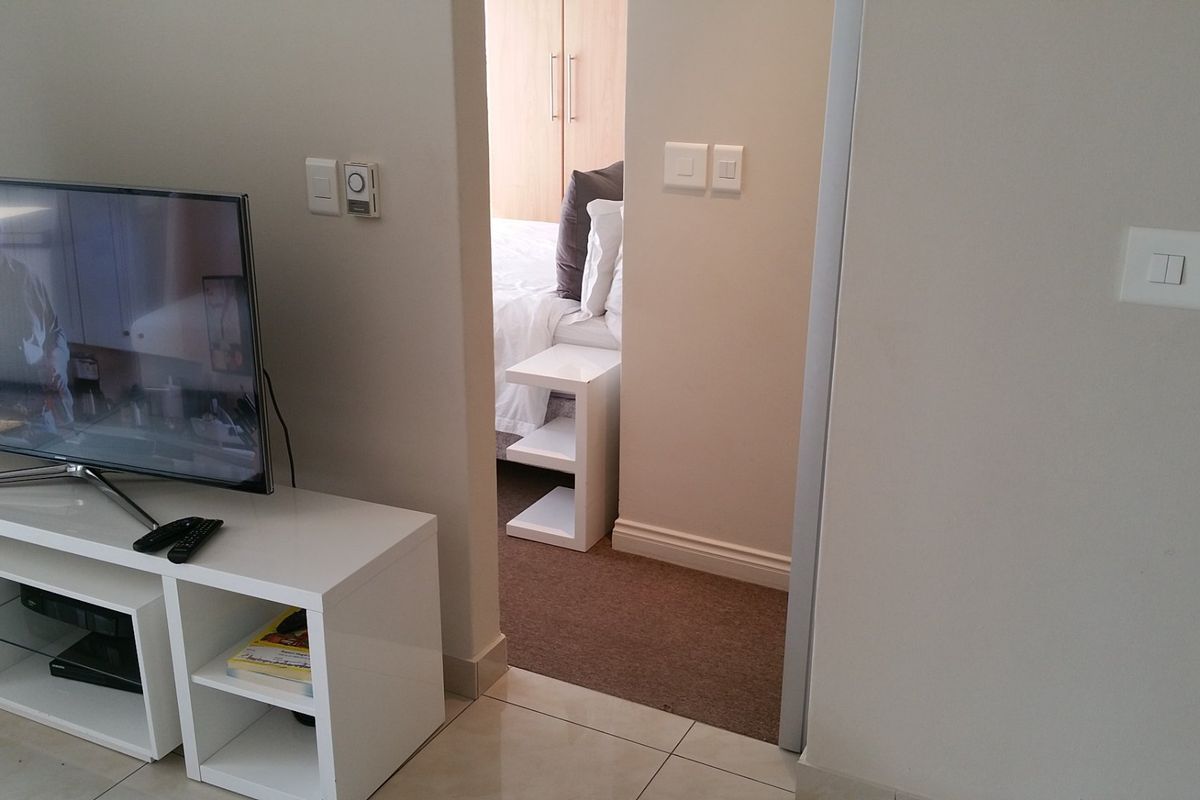 A view from the living area looking into a bedroom featuring built-in cupboards, tiled flooring in the main area, and carpeted flooring in the bedroom.
