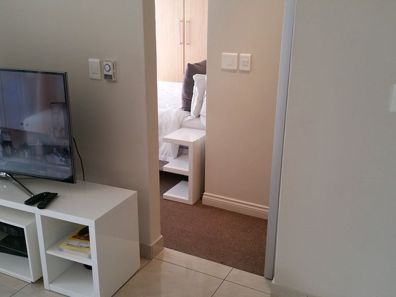 A view from the living area looking into a bedroom featuring built-in cupboards, tiled flooring in the main area, and carpeted flooring in the bedroom.
