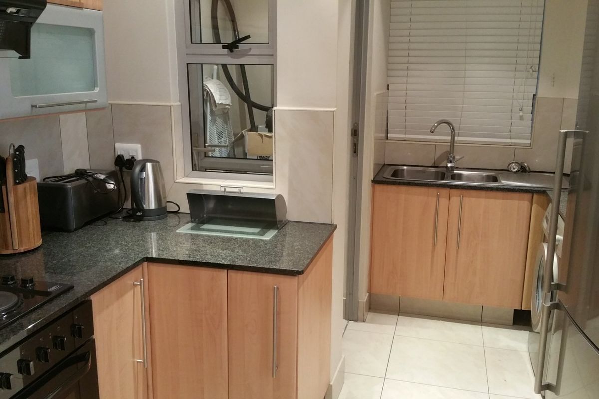 A functional kitchen featuring light wood cabinetry, granite countertops, a double basin sink, and integrated electric cooking appliances with tiled splashbacks.
