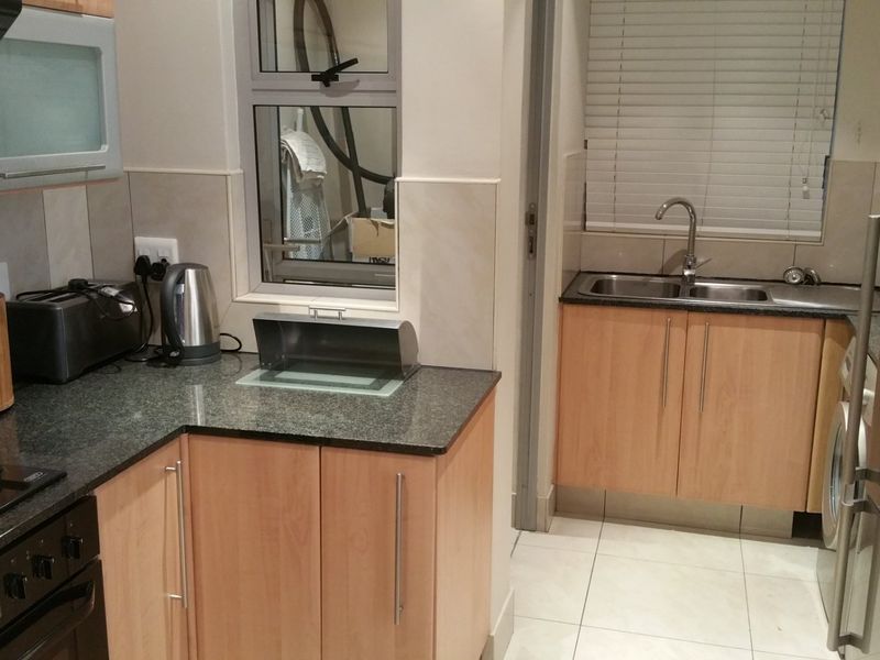 A functional kitchen featuring light wood cabinetry, granite countertops, a double basin sink, and integrated electric cooking appliances with tiled splashbacks.