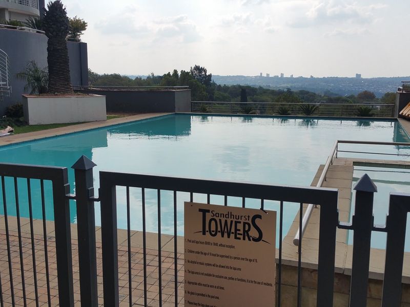 Communal swimming pool area featuring a paved deck, metal safety fencing, and elevated views of the surrounding landscape.