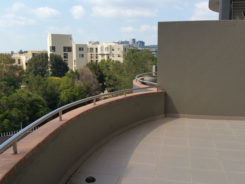 A spacious, open-air balcony featuring tiled flooring, a modern stainless steel railing, and elevated views of the surrounding neighborhood.