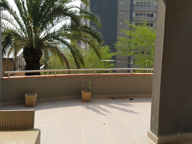 A spacious outdoor balcony featuring tiled flooring and a metal safety railing, offering an open-air space with views of the surrounding apartment complex.