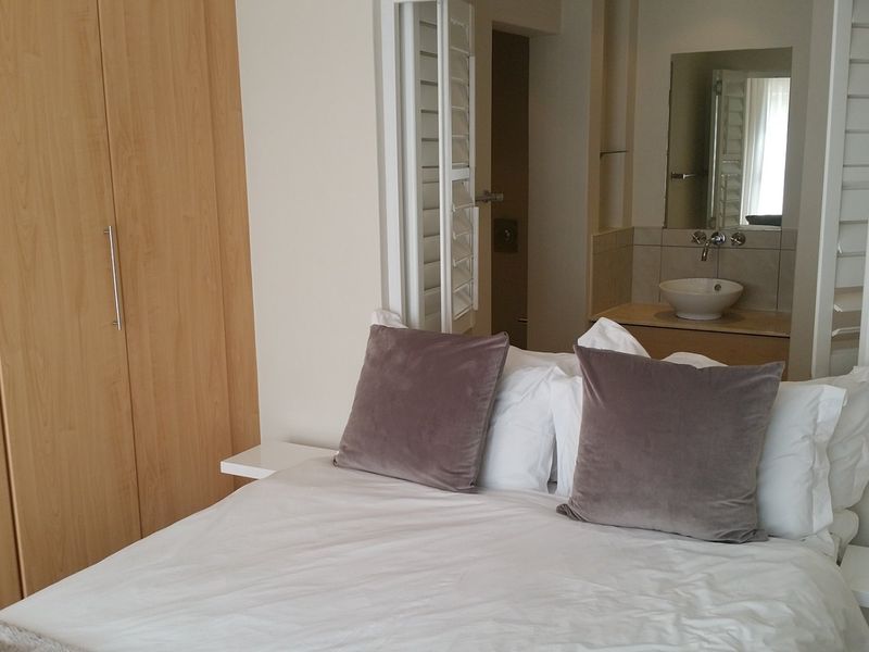 A bedroom featuring built-in wooden cupboards, floating bedside tables, and an open-plan en-suite bathroom with a modern vessel sink.