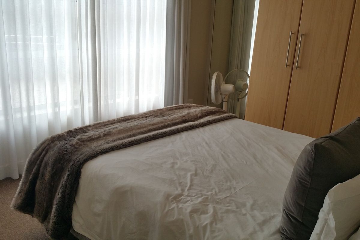 A bedroom featuring neutral carpet flooring, floor-to-ceiling sheer curtains, and a built-in wooden wardrobe.