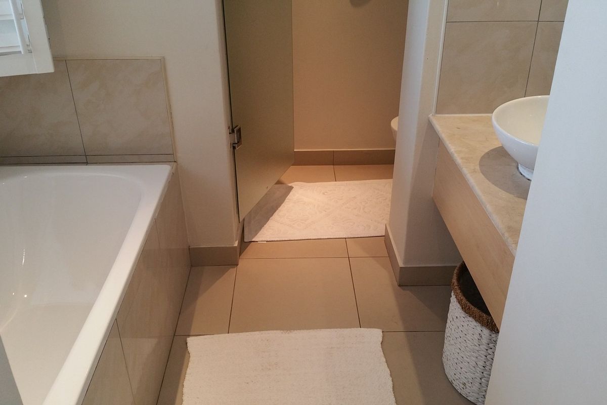 A functional bathroom featuring a built-in bathtub, a vanity with a stone countertop and basin, and neutral wall and floor tiling.