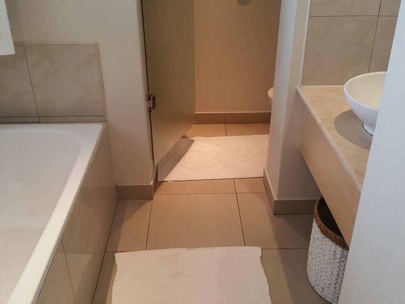 A functional bathroom featuring a built-in bathtub, a vanity with a stone countertop and basin, and neutral wall and floor tiling.