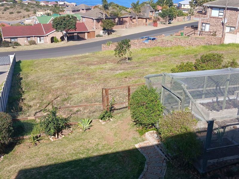 An elevated view of a residential vacant plot featuring a fenced garden area, mesh enclosure, and paved pathway with surrounding neighborhood views.