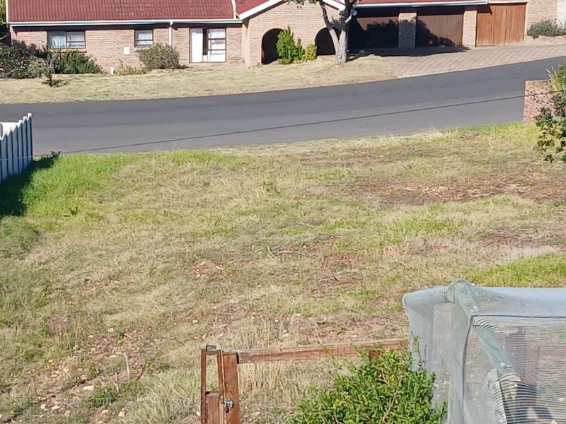 A view of a vacant residential plot of land with grass cover and boundary fencing, situated in a suburban street setting.