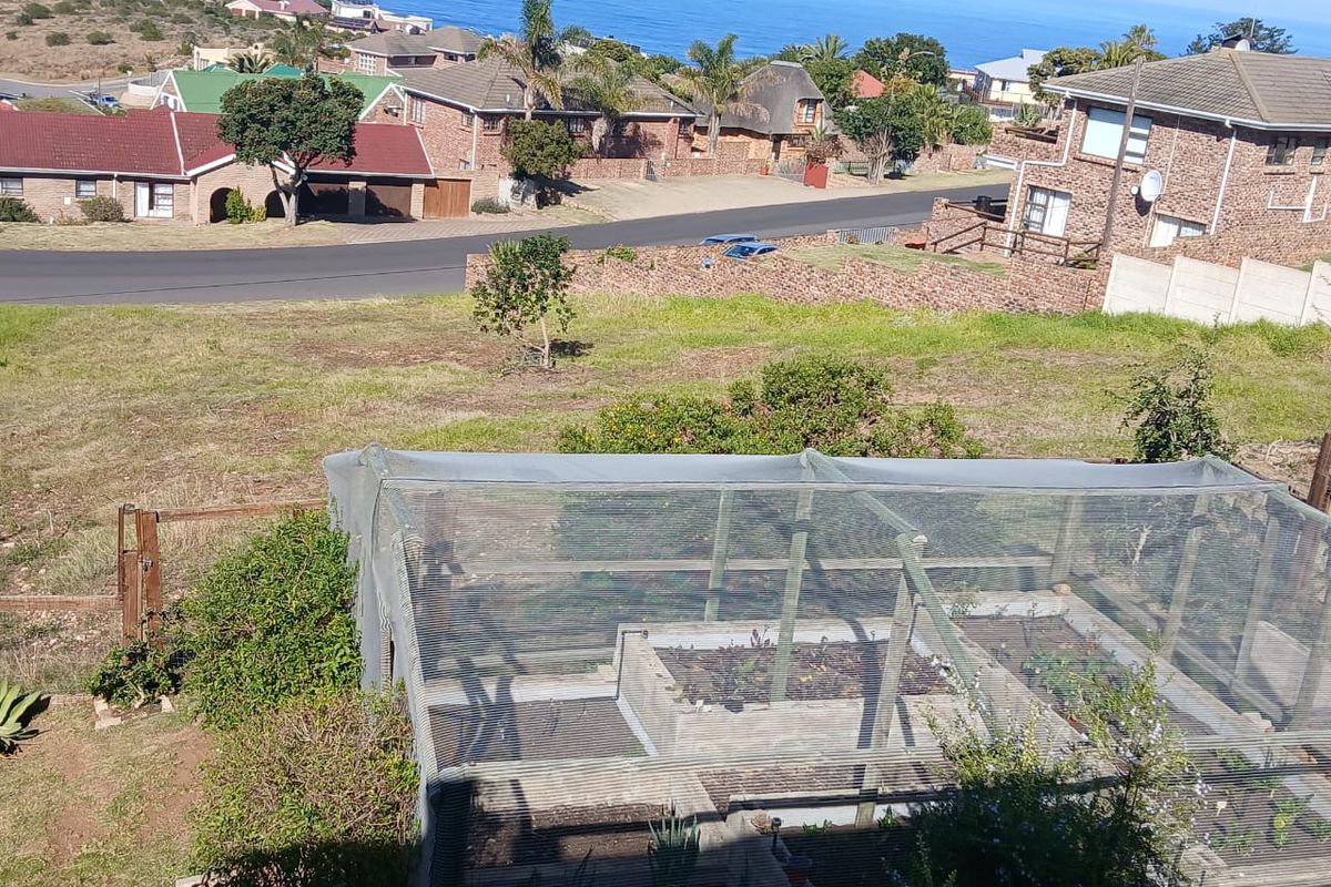 Elevated view of a residential plot featuring a netted garden structure with raised beds, overlooking the surrounding neighborhood and coastal landscape.