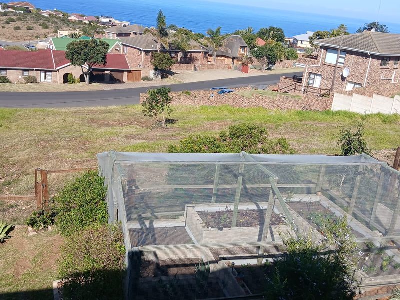 Elevated view of a residential plot featuring a netted garden structure with raised beds, overlooking the surrounding neighborhood and coastal landscape.