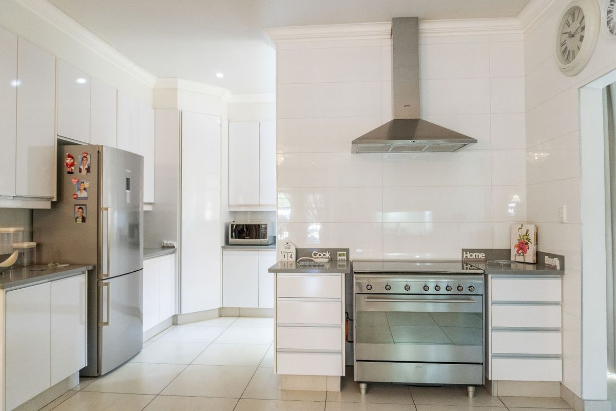 Modern kitchen featuring white cabinetry, stone countertops, stainless steel oven with extractor fan, and tiled flooring.
