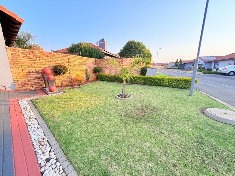 A well-maintained front garden featuring a manicured lawn, neat hedging, and a brick boundary wall with a paved walkway.