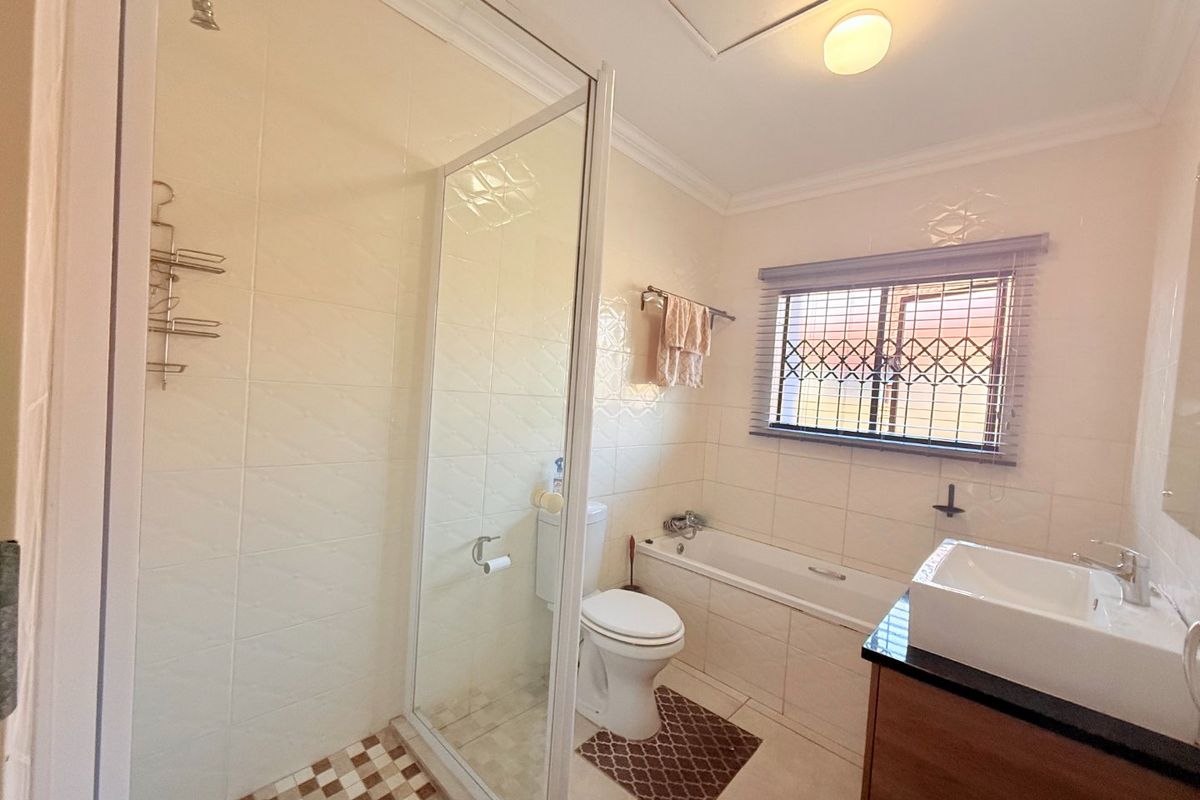 A functional bathroom featuring a glass shower enclosure, built-in bathtub, vanity with countertop basin, and tiled finishes.