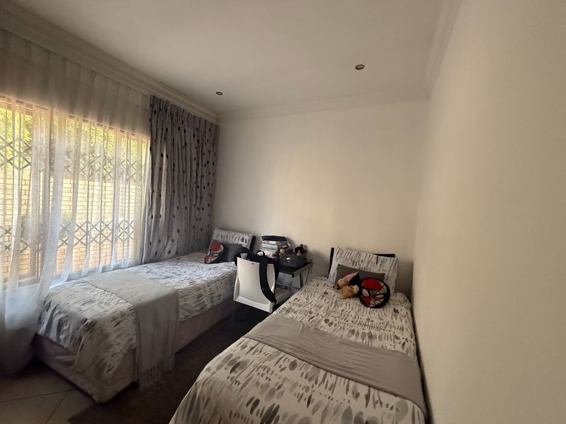 A functional bedroom featuring tiled flooring, recessed downlights, and a window fitted with a security gate and curtain tracks.