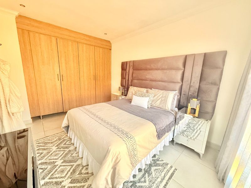 A well-maintained bedroom featuring light wood-finish built-in wardrobes, neutral tiled flooring, and recessed ceiling lighting.