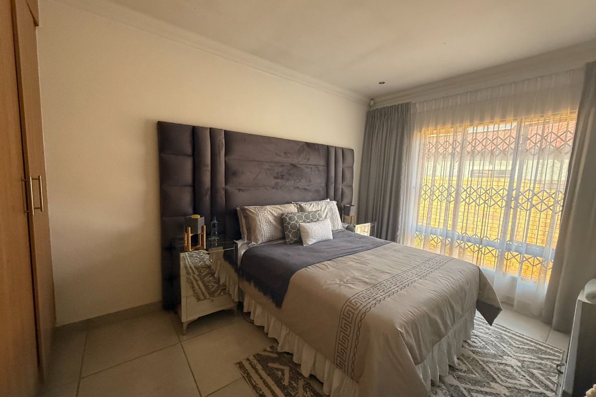 A well-maintained bedroom featuring tiled flooring, a built-in wardrobe, and a large window fitted with a security gate for added safety.