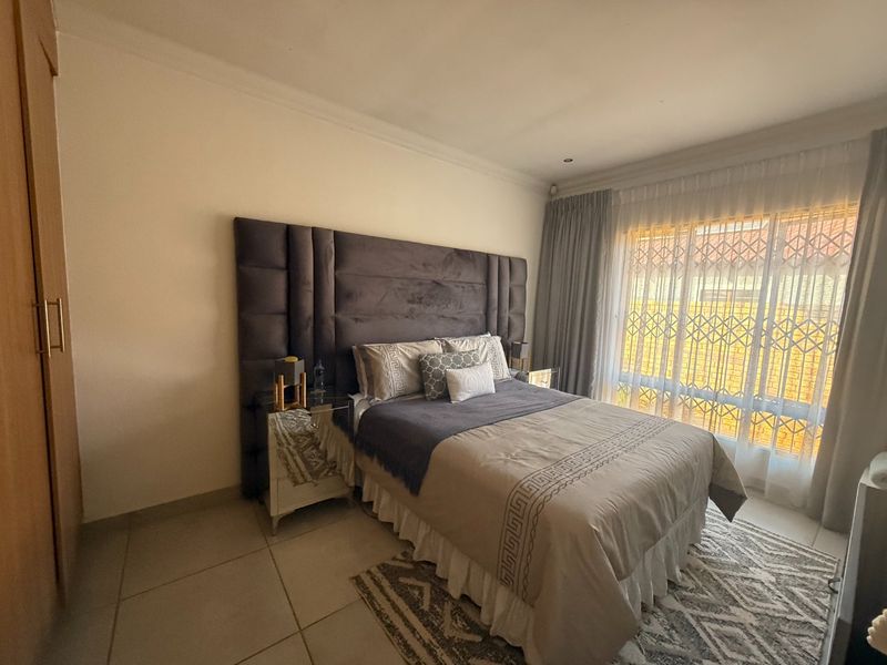 A well-maintained bedroom featuring tiled flooring, a built-in wardrobe, and a large window fitted with a security gate for added safety.