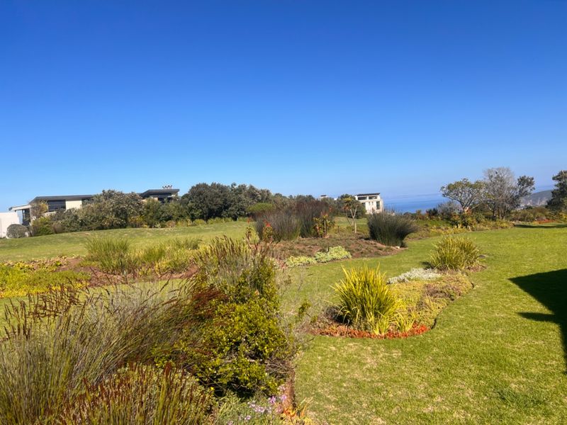 A well-maintained landscaped garden featuring lush green lawns and native shrubbery, offering a serene outdoor space with distant coastal views.