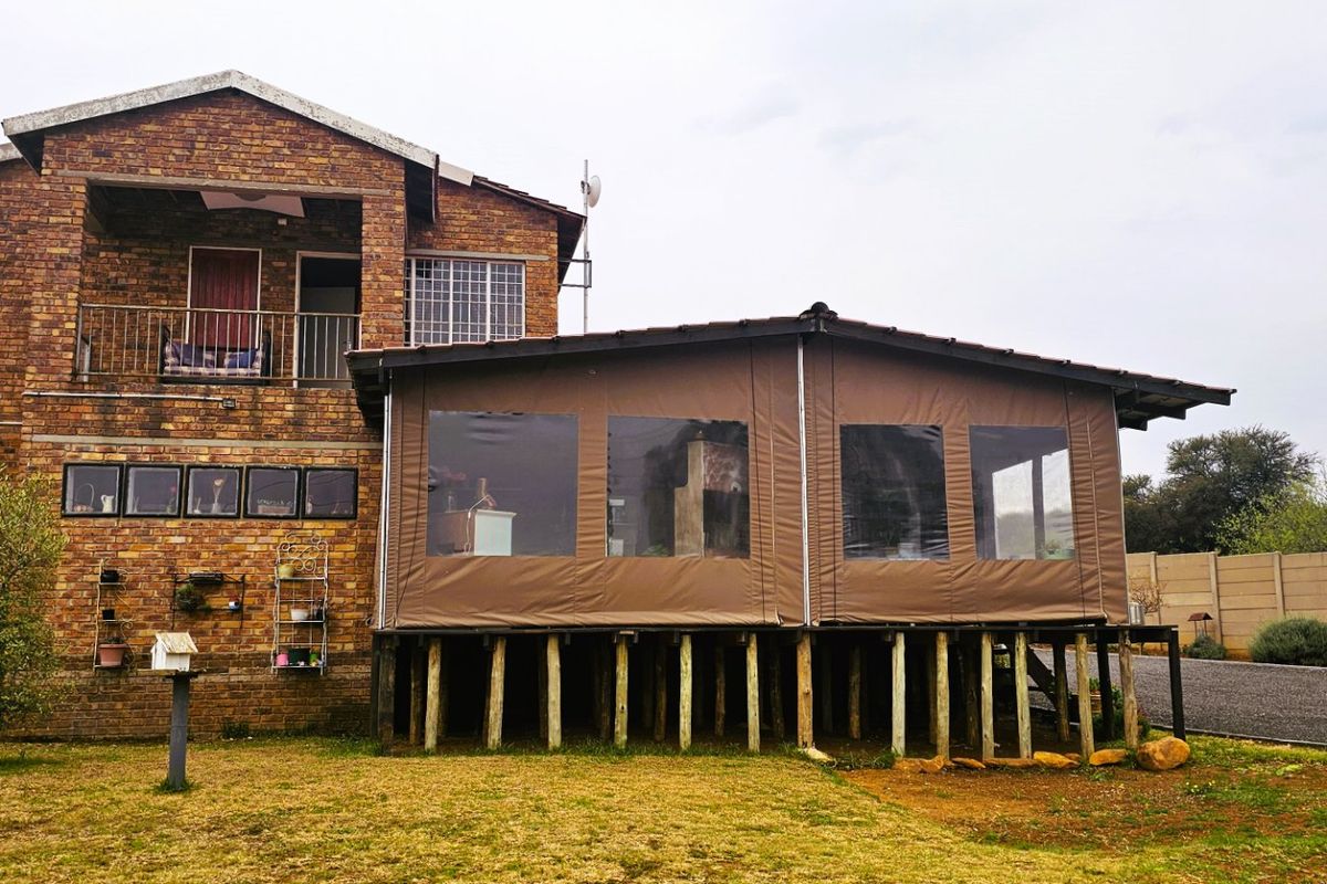 Rear view of a multi-story face brick house featuring an elevated timber deck with an enclosed patio area and an upper-level balcony.