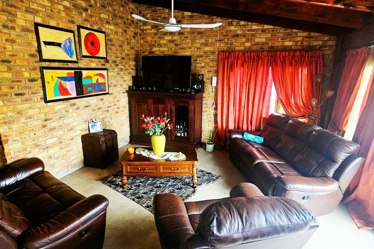 A cozy living room featuring exposed brick walls, a vaulted timber ceiling with a ceiling fan, and tiled flooring.