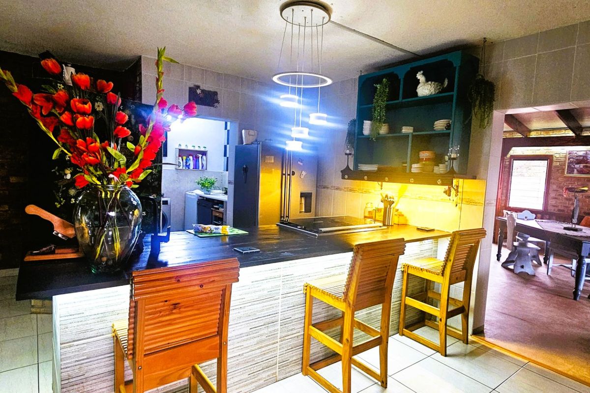 A well-lit kitchen featuring a central island with a built-in hob, tiled flooring, and an exposed brick accent wall.