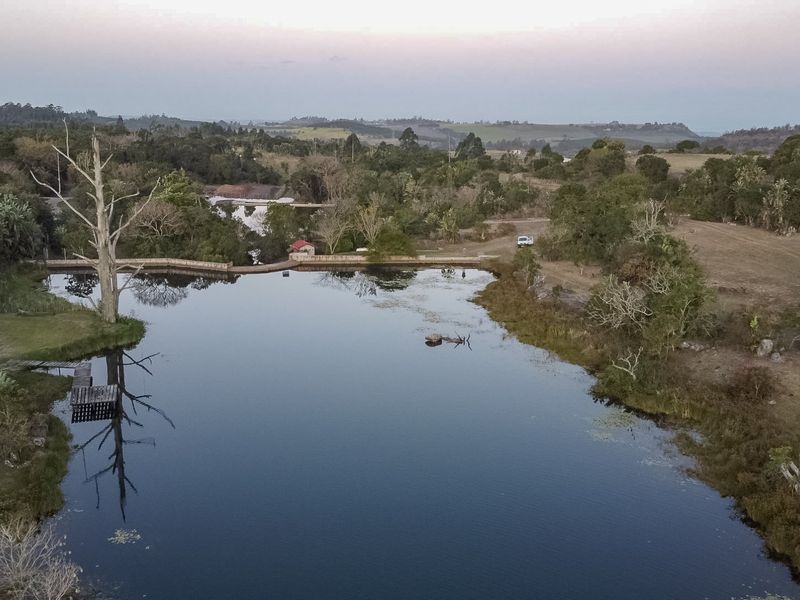An aerial view of a tranquil farm dam surrounded by natural landscape, featuring a small wooden jetty and lush greenery.