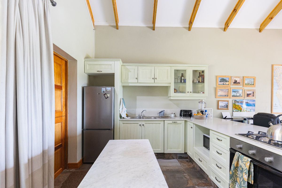 A rustic kitchen featuring light-toned cabinetry, stone flooring, exposed timber ceiling beams, and a built-in oven with a gas cooktop.