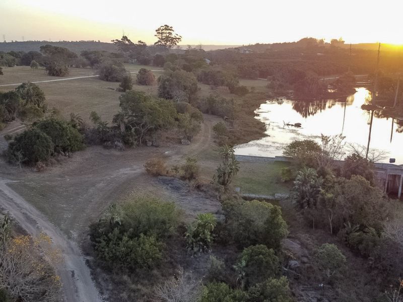Aerial view of the farm property featuring expansive natural landscape, mature trees, and a scenic dam at sunset.