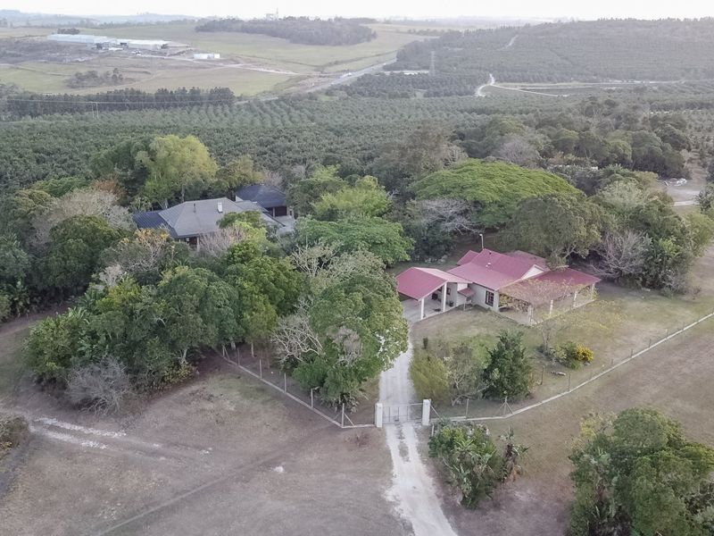 Aerial view of a farm property featuring a main residence with a red roof, surrounding mature trees, and expansive agricultural land.