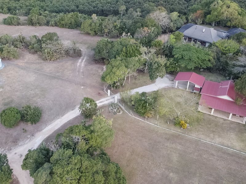 Aerial view of a farm property featuring multiple buildings, a gravel driveway, water storage tanks, and surrounding mature trees and open land.