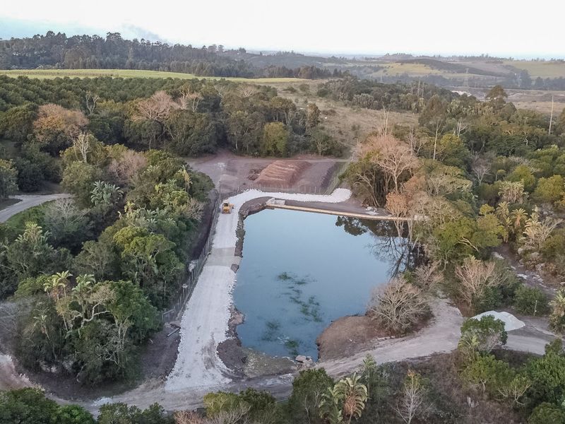 Aerial view of a farm property featuring a large dam, surrounding indigenous vegetation, and established orchard areas with gravel access paths.