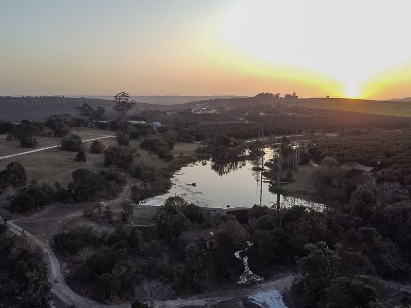 An expansive aerial view of the farm property featuring a serene lake, surrounding orchards, and natural landscape at sunset.