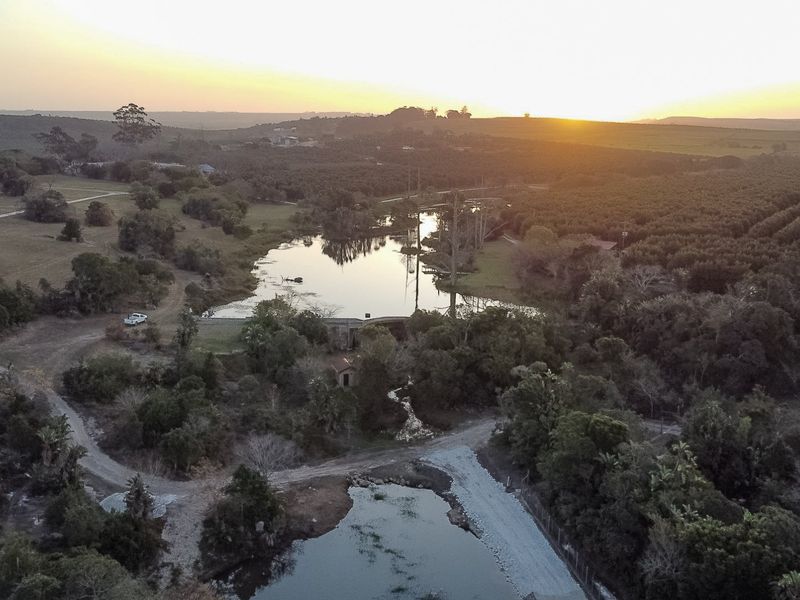 Aerial view of the farm property featuring a scenic dam, surrounding orchards, and natural landscape at sunset.