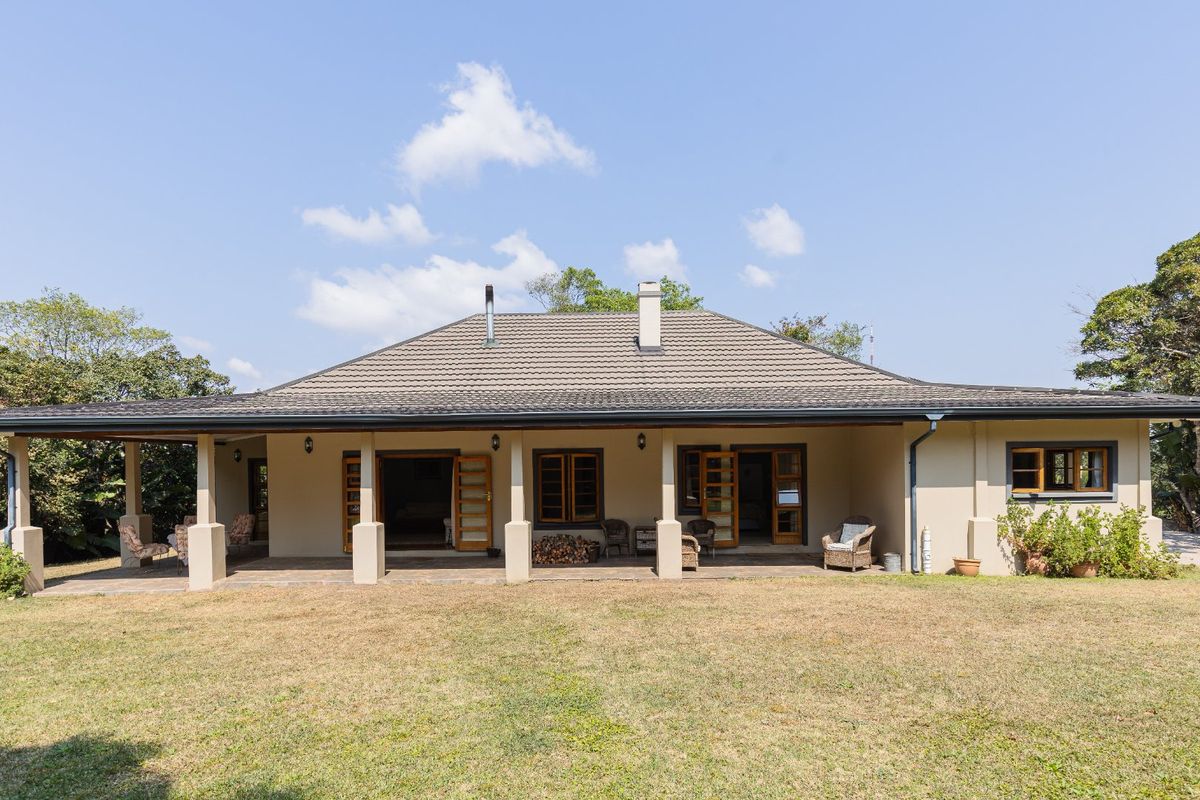 A spacious rear exterior view of the farmhouse featuring a wide covered patio, tiled roof, and direct access to the garden through multiple timber doors.