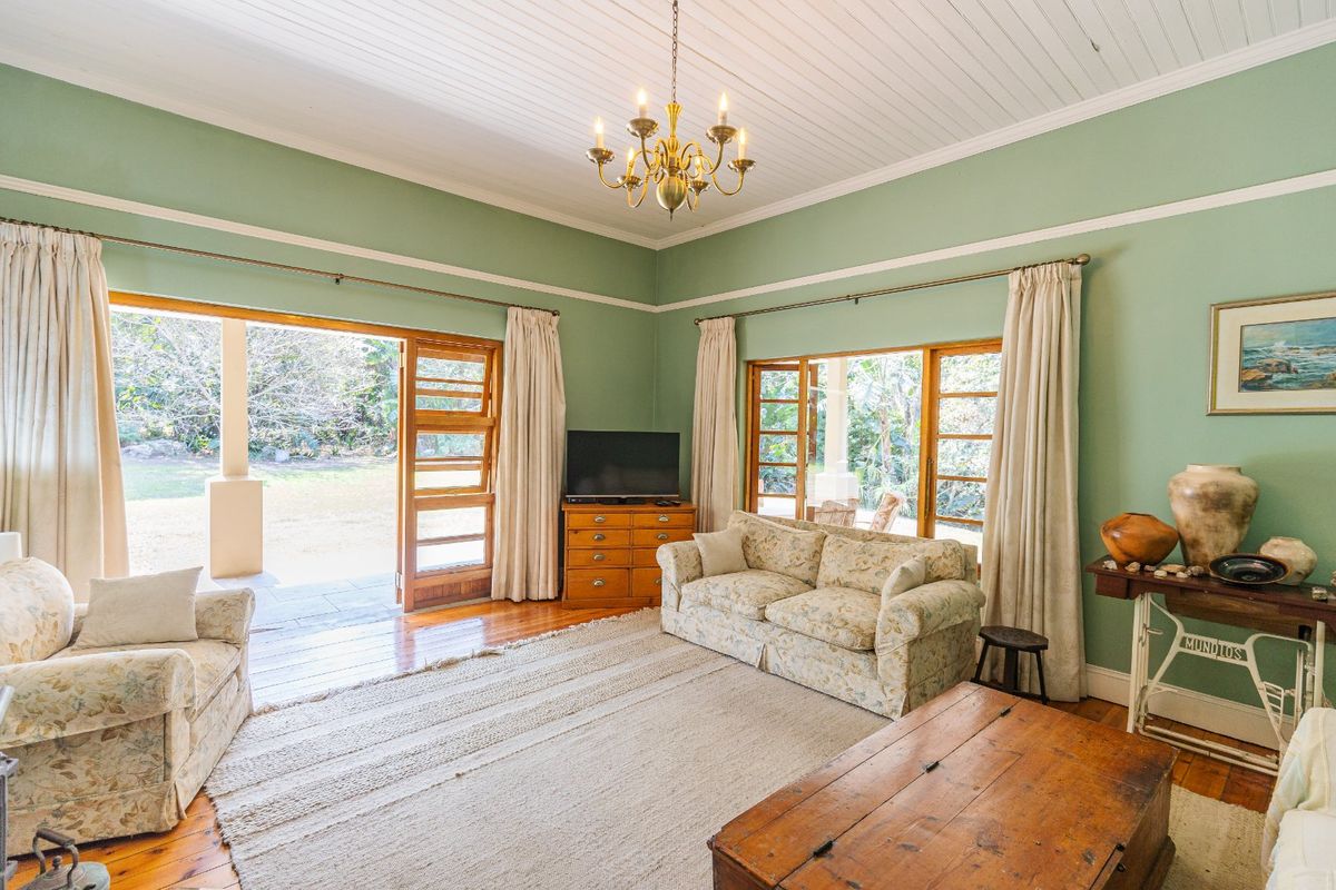 A bright living room featuring timber flooring, high tongue-and-groove ceilings, and large wooden doors opening onto a covered patio area.