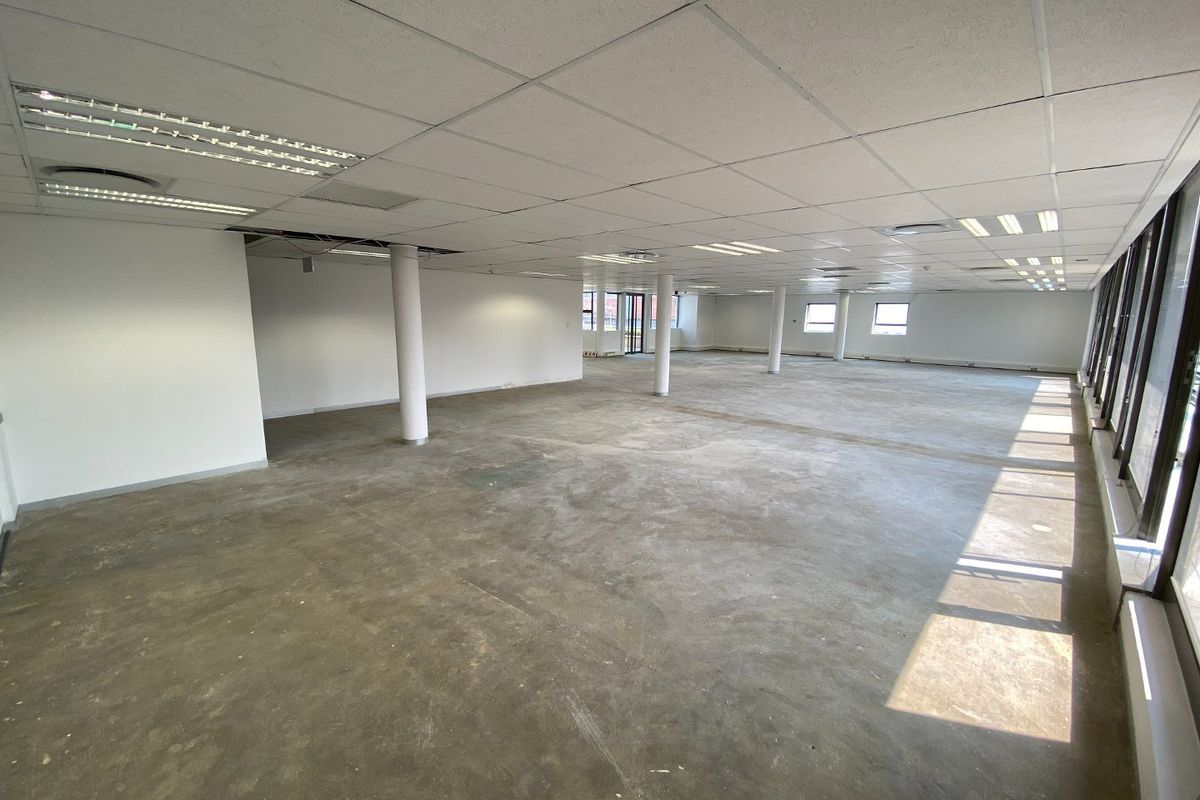 Spacious open-plan commercial office area featuring large windows, structural columns, and a suspended ceiling, currently in a shell condition ready for fit-out.
