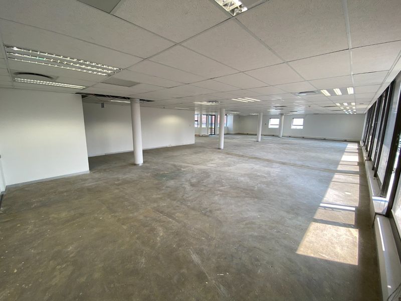 Spacious open-plan commercial office area featuring large windows, structural columns, and a suspended ceiling, currently in a shell condition ready for fit-out.