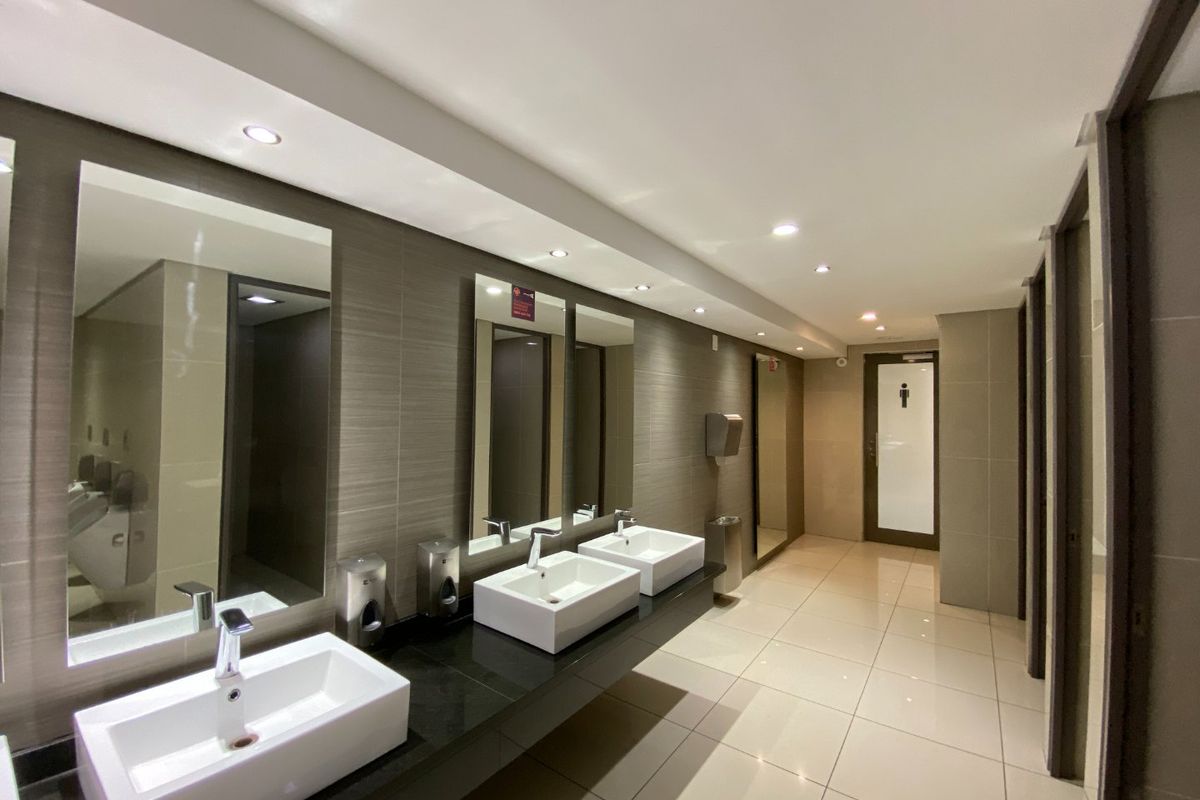 Modern commercial restroom featuring a sleek granite vanity with multiple vessel sinks, recessed lighting, and high-quality tiled finishes throughout.