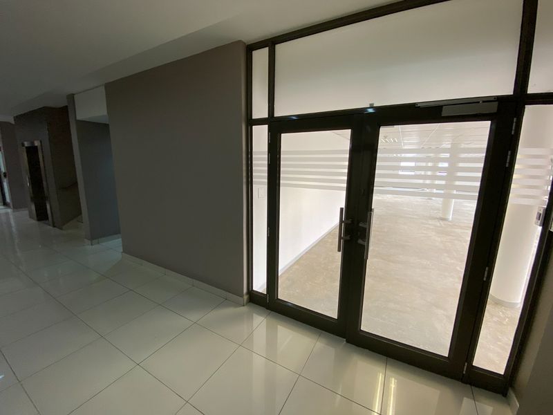 A modern commercial office entrance featuring glass double doors, polished tile flooring, and clear access to an open-plan interior space.